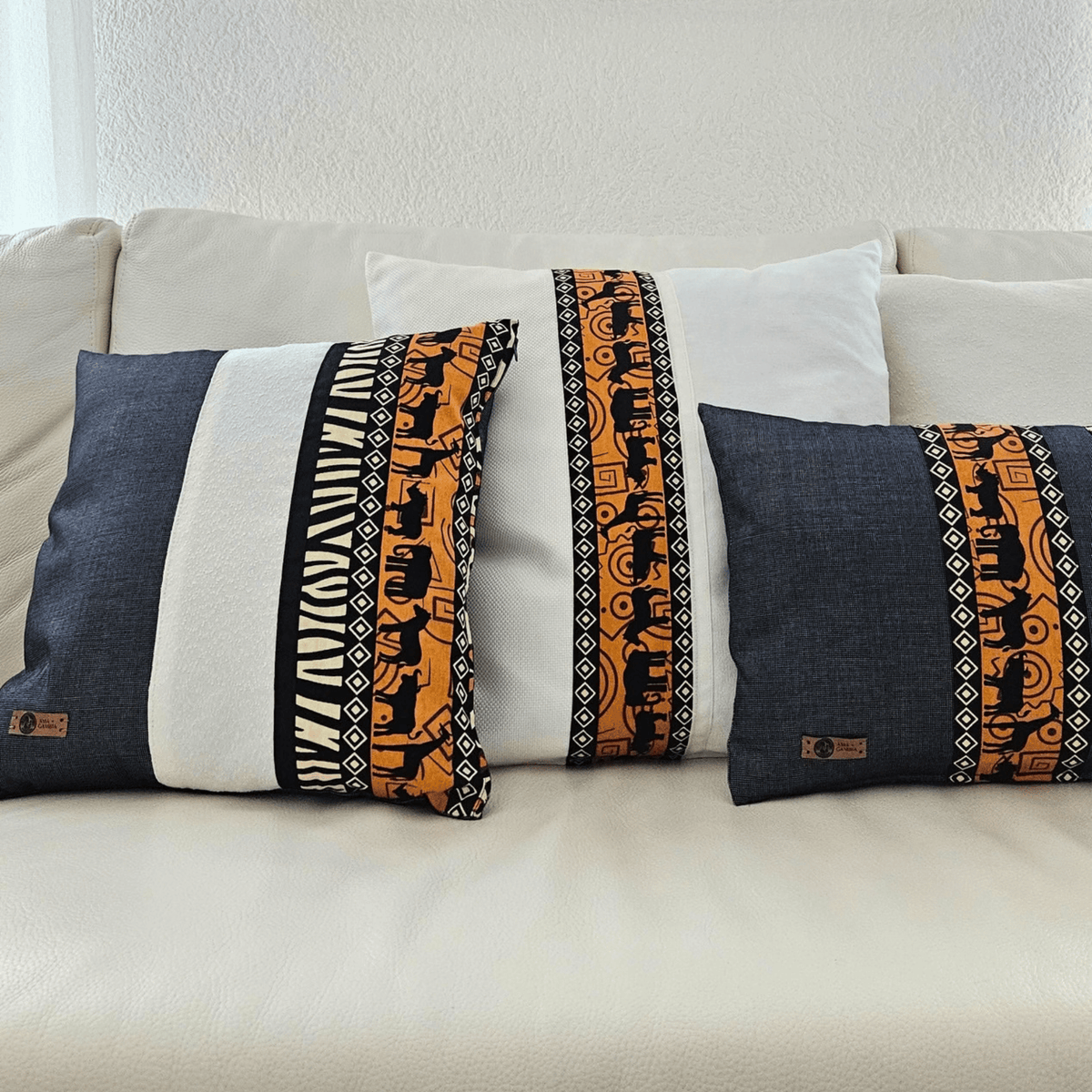 Image de trois coussins en tissu wax avec motifs d'animaux, sur un canapé blanc