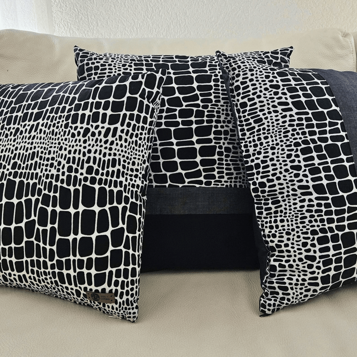 Image de trois coussins en tissu wax noir et blanc posé sur un canapé blanc